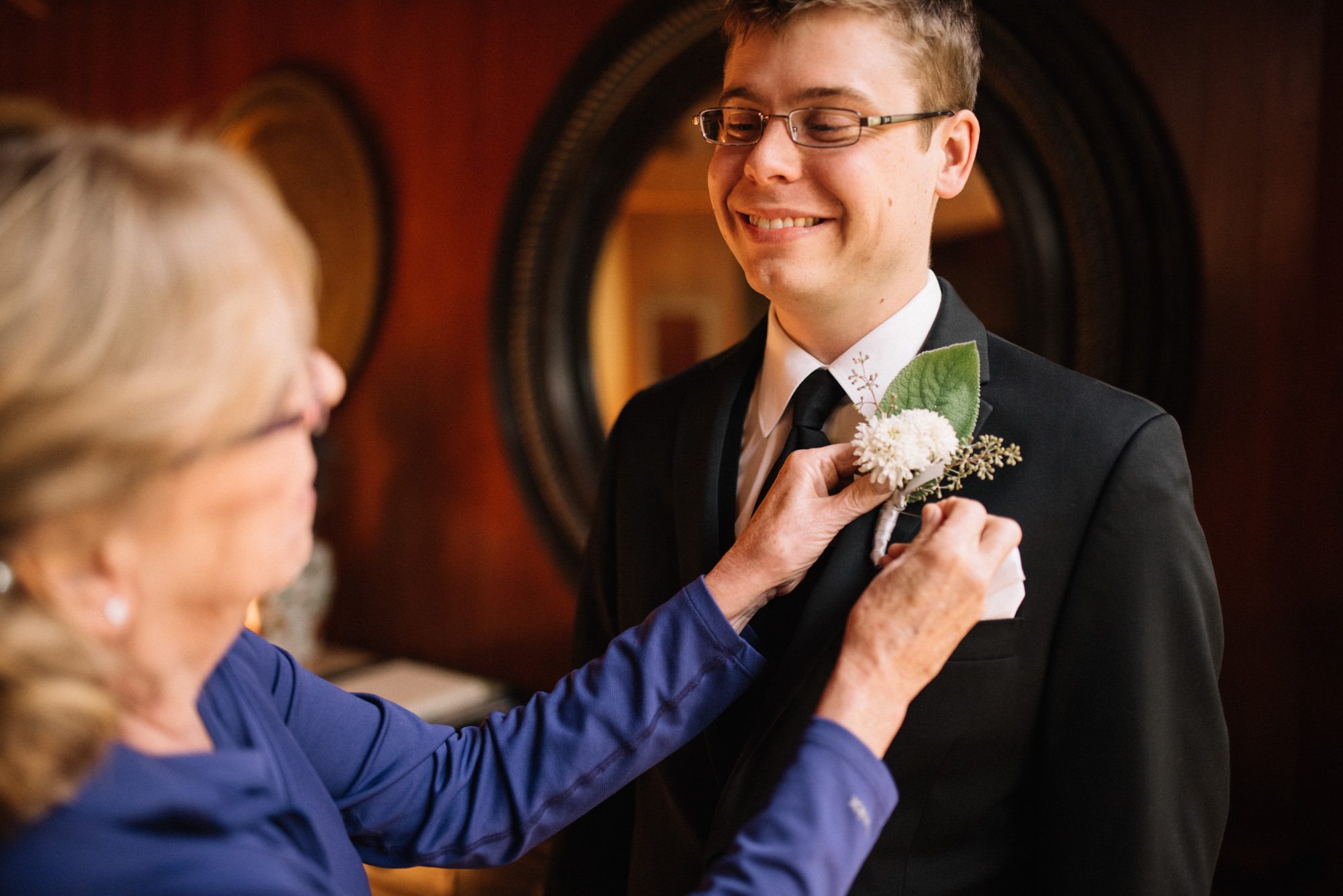 Graeme's mom helps him with a boutonniere while he gets ready for his wedding at Kingston House, Washington.